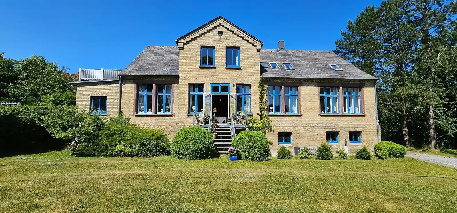 Das Haus Magnussen in Schleswig: Backsteinbau mit blau gefassten Fensterrahmen und Staffelgiebel, davor eine weite Parkanlage.